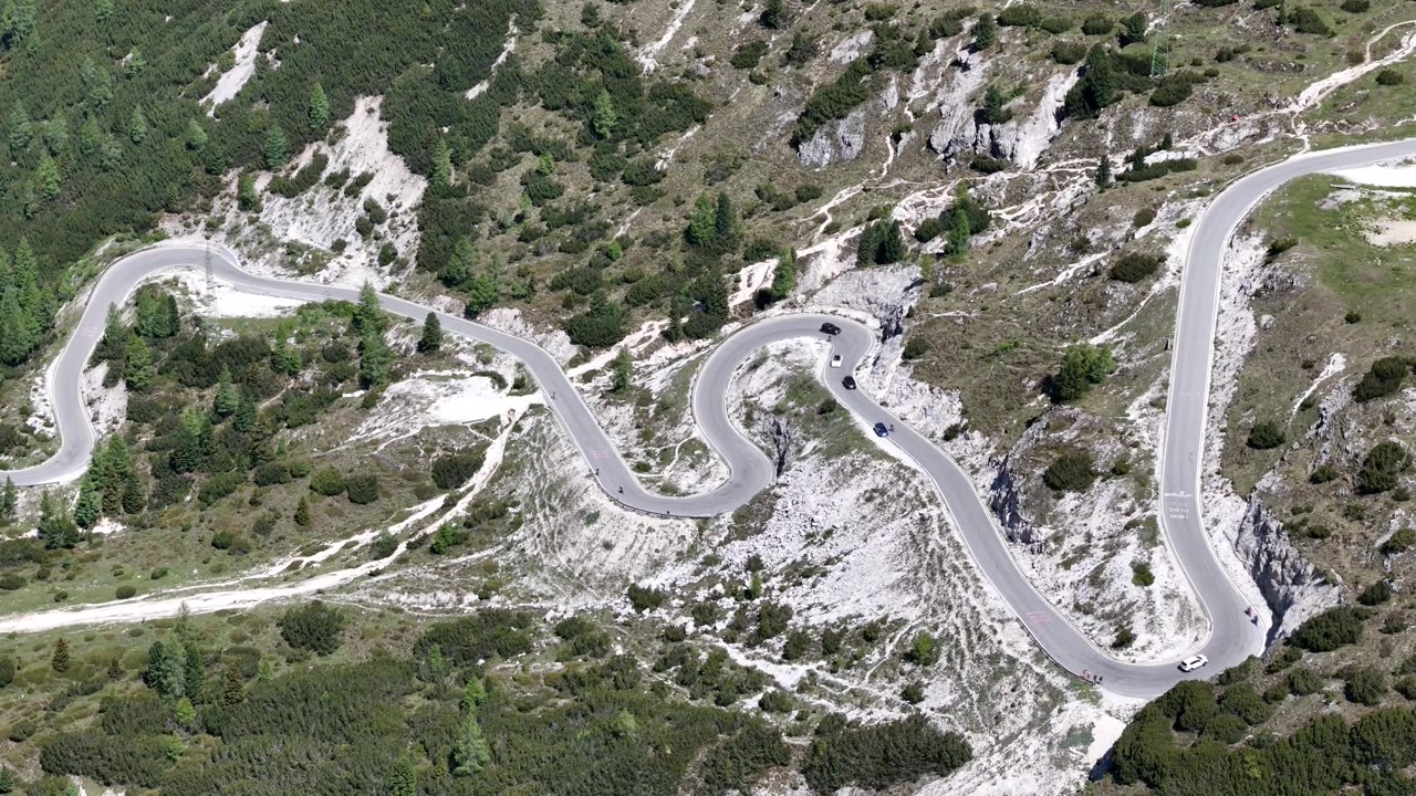 Breathtaking 4K drone footage revealing cars snaking up the spectacular winding road cutting through the rugged Dolomites landscape towards the iconic Tre Cime di Lavaredo, Italy.