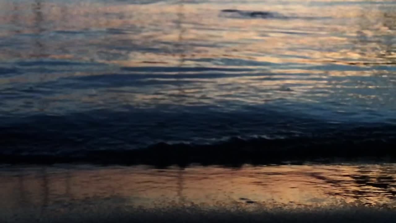 Close up and slow motion of waving water of a peaceful sea reflecting light at the beach during sunset on a quiet evening