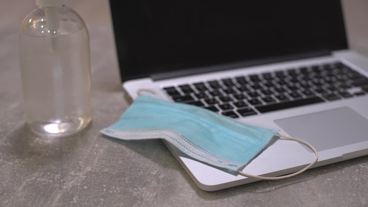 computadora portátil con máscara facial médica, bloc de notas y lápiz en la parte superior junto con una taza de café en la mesa de comedor. configuración en el hogar. concepto de trabajo en el hogar.