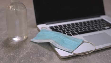 computadora portátil con máscara facial médica, bloc de notas y lápiz en la parte superior junto con una taza de café en la mesa de comedor. configuración en el hogar. concepto de trabajo en el hogar.