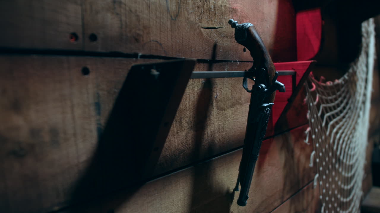 An antique flintlock pistol is mounted on a rustic wooden wall beside a section of fishing net. Vintage firearm and nautical decor of a maritime pirate ship