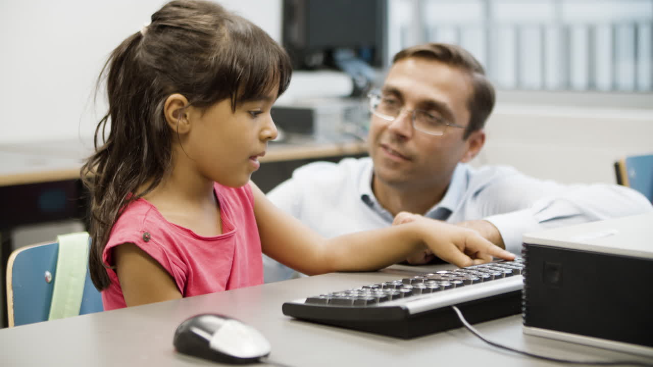 profesor sentado junto a la niña, enseñándole a escribir en el teclado