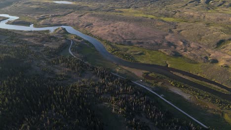 aerial footage shows calm river curving through open grassland and forest in west virginia during sunset, highlighting natural textures, tree shadows, clear water, and peaceful terrain below