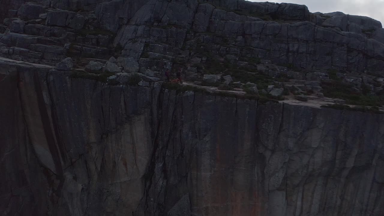 Steep cliffside in Norway with rocky formations and green vegetation on top