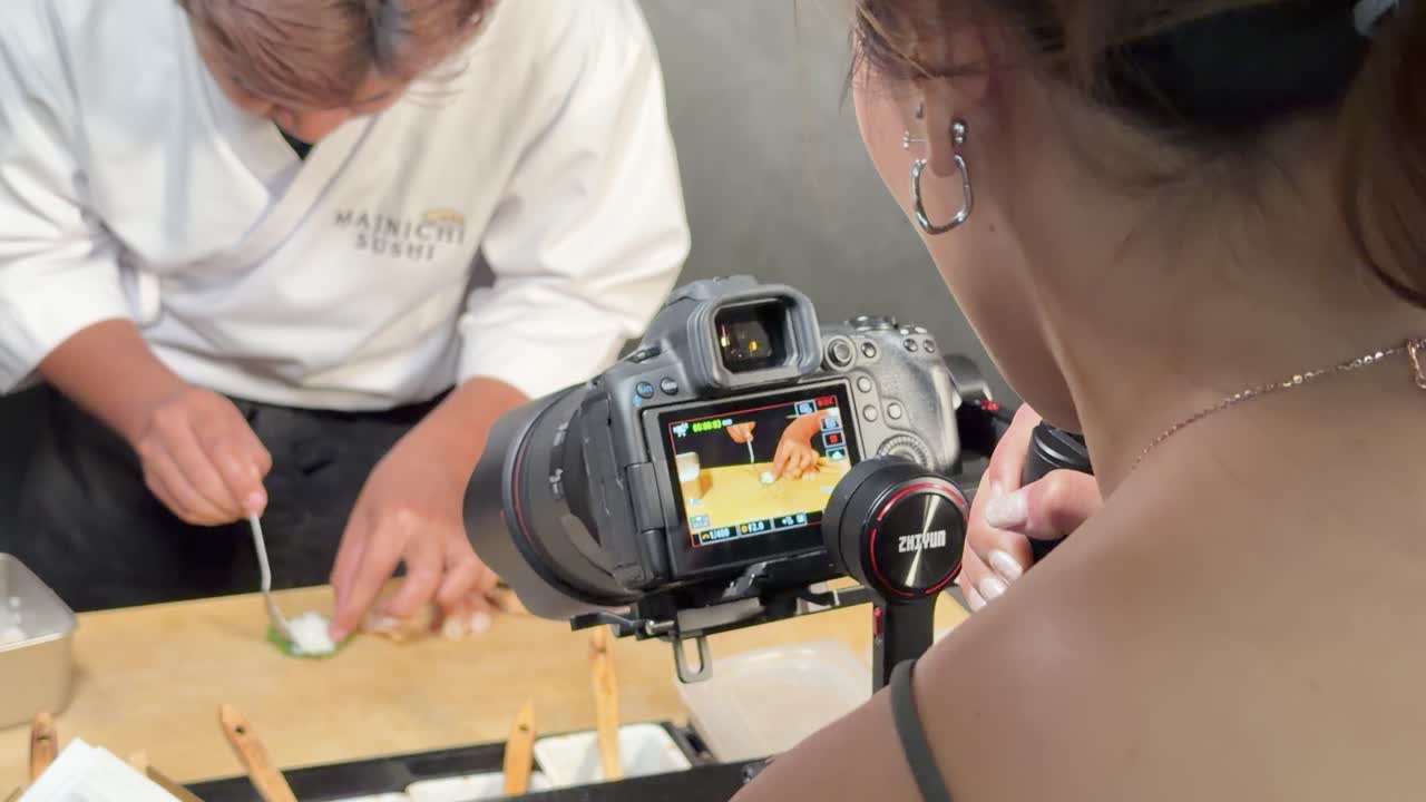 Food vlogger records sushi chef slicing cucumber garnish at restaurant counter with close-up camera