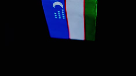 Studio-lit Uzbekistan flag gently flutters against a dramatic black backdrop
