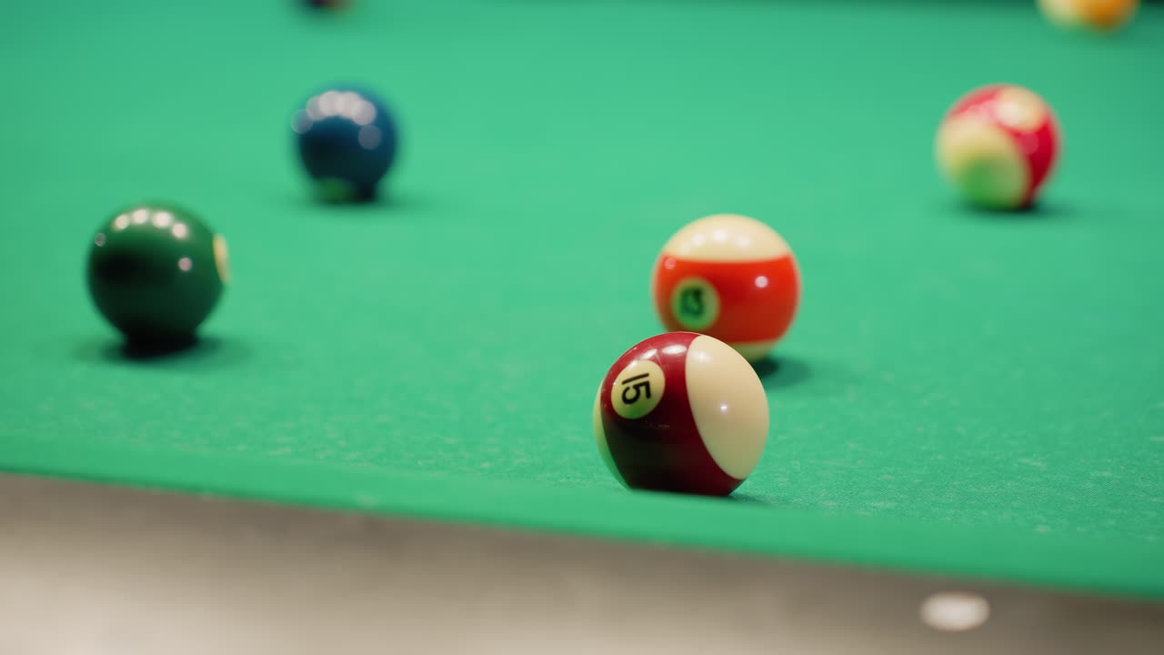 White billiard ball rolls across green pool table after making contact with another ball. Vibrant pool balls scattered across surface capture dynamic motion of gameplay, showcasing precision