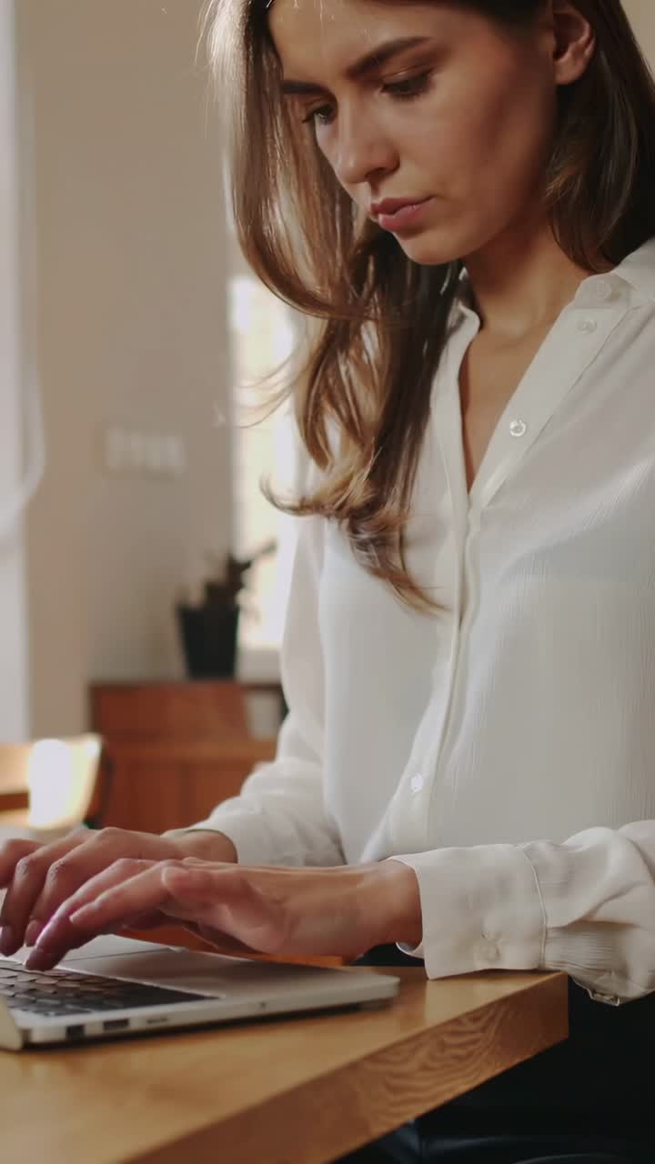 Video verticale: clip che inizia con un portatile sul bancone della cucina, una donna con una camicia bianca che digita, che lavora