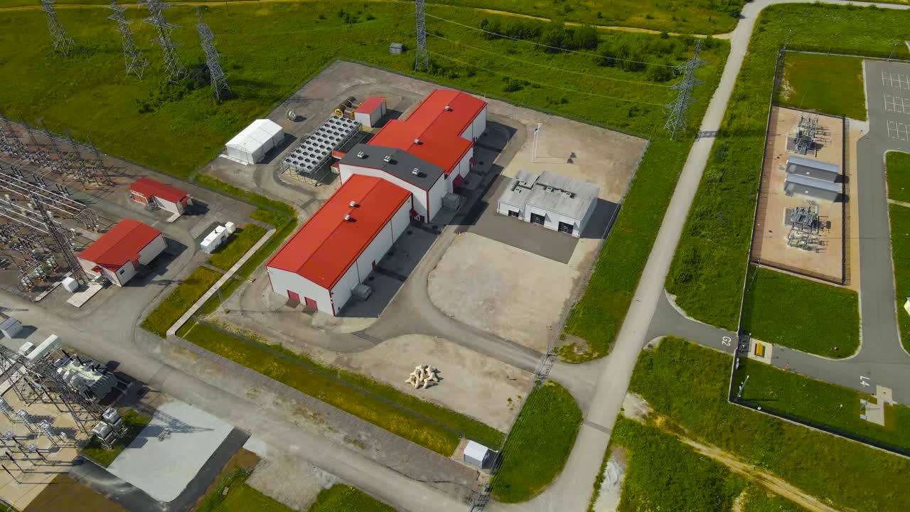 Aerial drone footage orbiting around a electrical substation with high voltage electrical lines that are powering a large modern data centre next to the building during a summer sunny day, countryside