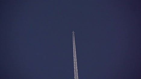 upward footage of an airplane leaving two white plumes of condensation from its jet engines against a clear blue sky