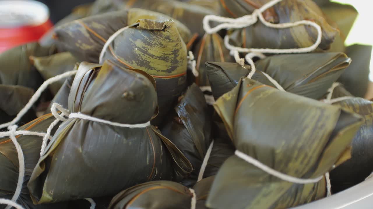 Traditional chinese food Zongzi or Zong close-up. Zongzi is rice dish made of glutinous rice stuffed with different fillings and wrapped in bamboo leaves. Local street food market. High quality 4k footage