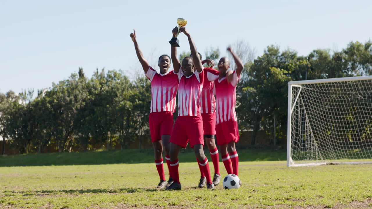 Celebrating victory, male soccer team holding trophy on field with soccer ball