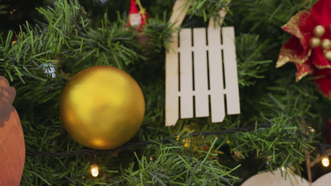 Close-up of beautifully decorated Christmas tree with glowing fairy lights, golden baubles, red poinsettia, wooden ornaments, and blurred bokeh lights in the background