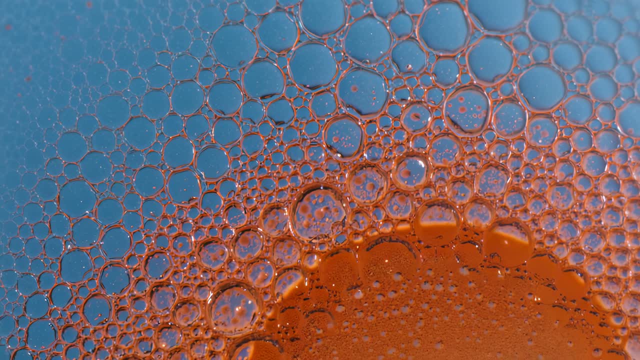 Pellicola che drena causando dense bolle sferiche che si fondono lungo il bordo del liquido arancione in un'impostazione macro.