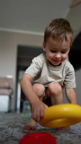 cute caucasian toddler plays joyfully with the rings from toy pyramid. a black cat comes up to the camera and a boy. low angle view. vertical video.