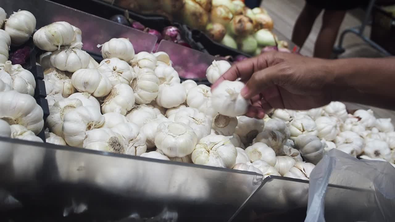 식료품점의 신선한 농산물 섹션에서 마늘 머리를 고르는 쇼핑객