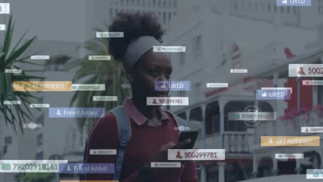 Animation-of-social-media-notifications-over-african-american-woman-using-smartphone-in-city-street