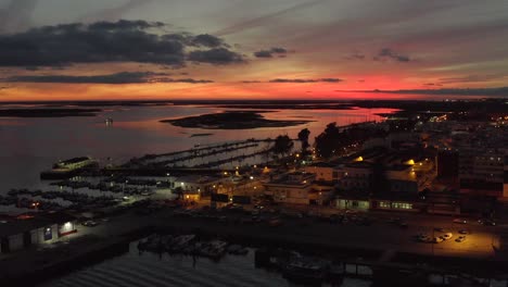 epic incredible pink and orange sun setting over beach town with street and city lights on, olhao city, portugal