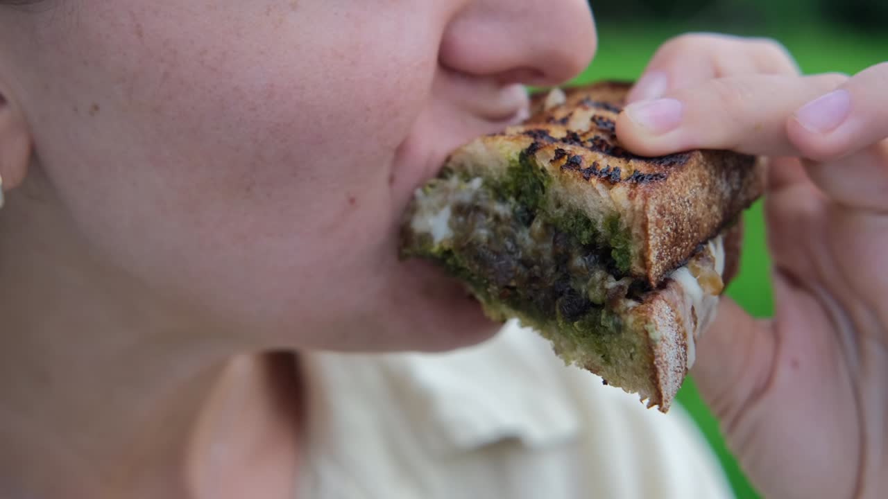 close up de una mujer comiendo un delicioso sándwich tostado a la parrilla con queso derretido en la naturaleza, fuera del restaurante. almuerzo en una fiesta fresca, un descanso para almorzar para tomar un descanso del trabajo en la oficina