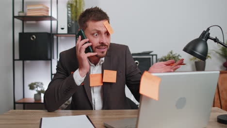 tired sad exhausted businessman working on laptop at office with many sticker tasks, panic attack