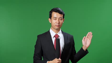 asian male tv news reporter in formal wear talking on a green screen, chroma key