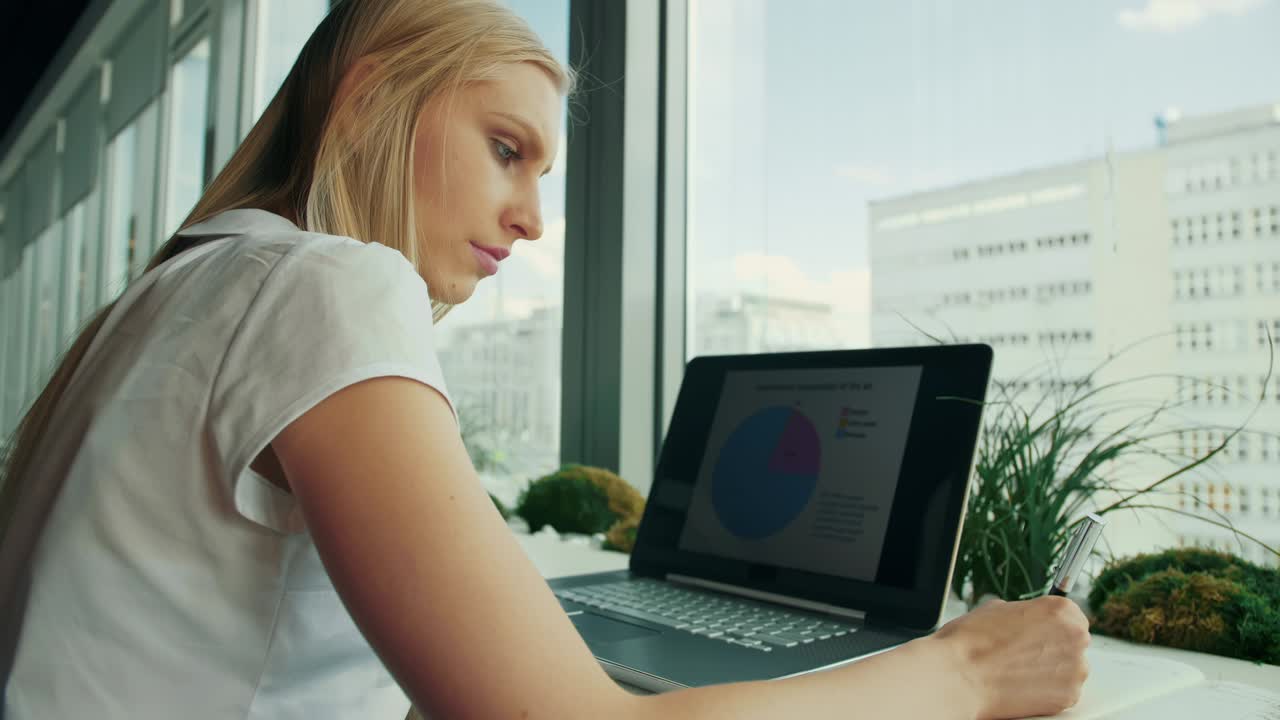 mujer de negocios trabajando con una computadora portátil en una nueva oficina. vista lateral de una mujer sentada en una mesa junto a una ventana en una oficina moderna y usando una computadora portable a la luz del día
