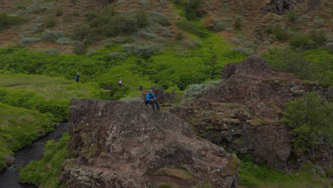 Drohnenansicht-Mann-Sitzt-Auf-Einem-Berggipfel-In-Island-Und-Blickt-Auf-Ein-Erstaunliches-Panorama,-Das-Sich-Frei-Fühlt.-Luftbild-Touristen-Wanderer-Auf-Felsformationen-Meditierend-Und-Beobachten-Die-Atemberaubende-Isländische-Landschaft