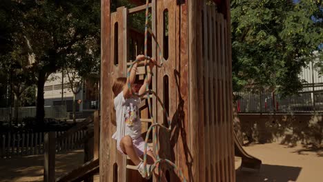 caucasian long haired blonde girl plays in the sandbox playground climbing a net