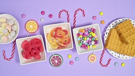 stop motion flat lay of sweet colorful candies and lollipops appear on pastel purple background. stop motion flat lay