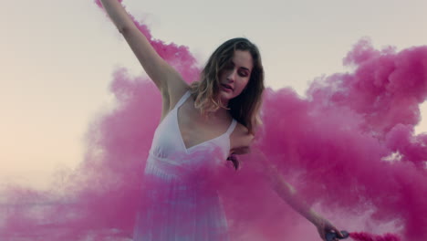 beautiful woman waving pink smoke bomb dancing on beach at sunrise celebrating creative freedom