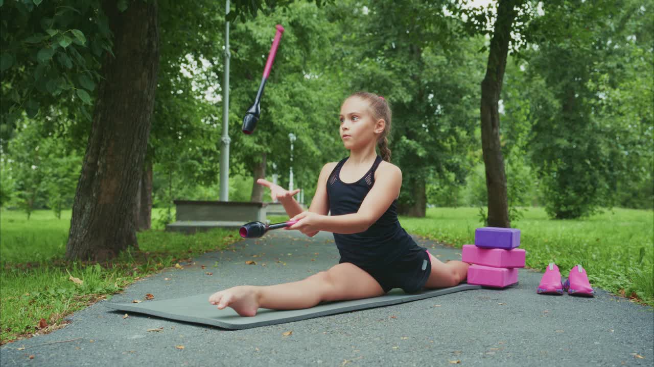 A Young Athlete Perfects Her Flexibility Routine on a Mat in a Lush Green Park, Featuring Colorful Training Equipment and a Focused Expression