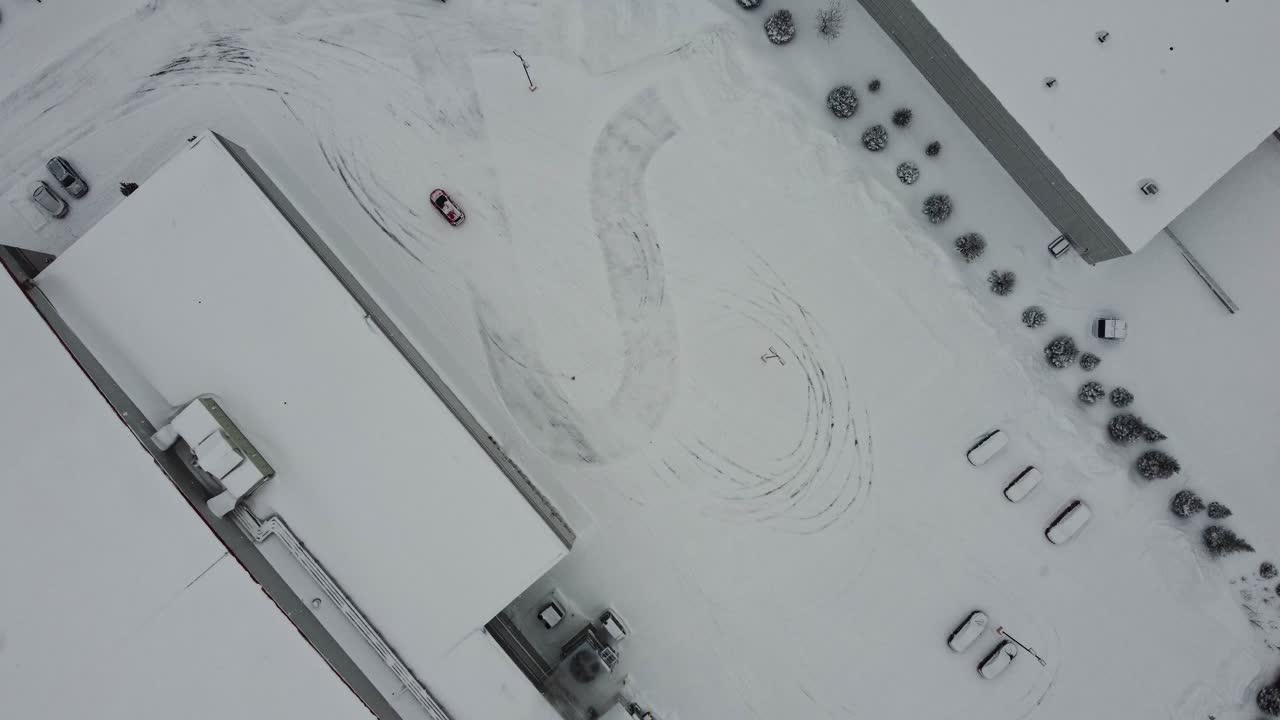 눈 덮인 주차장에서 스릴 넘치는 드리프트를 선보이며 인상적인 운전 기술을 선보이는 빨간 자동차의 매혹적인 드론 영상을 감상하세요.