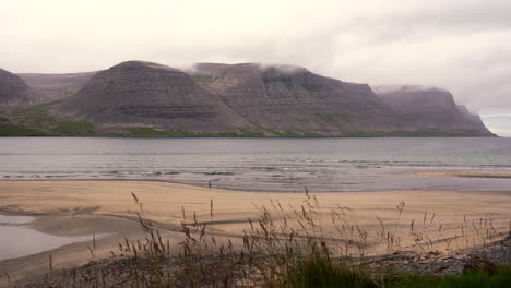 Moody-scenery-of-mountains,-beach-and-girl-walking-on-shore