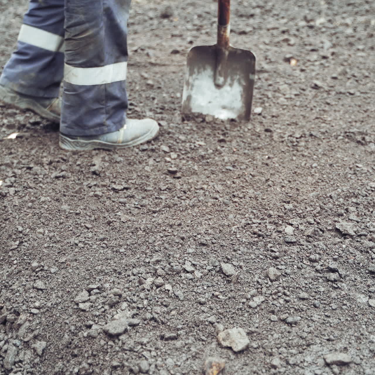 Legs of workers in protective uniform and boots with shovels leveling up the road. Team of workers preparing the ground for making new asphalt on a street. Close-up