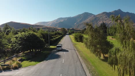 slowmo - luxury minivan driving on the road near arrowtown and queenstown, new zealand with mountains in background