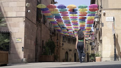 Cute-teen-girl-happily-running-down-a-street-covered-in-colorful-umbrellas-in-summer-sunshine