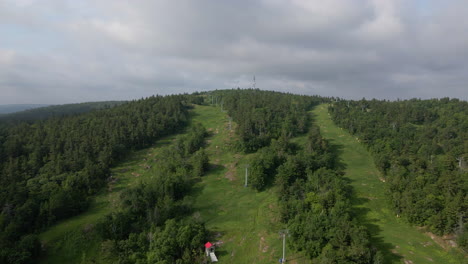 aerial footage flying up thick green tree covered mountain following chairlift on cloudy, overcast summer day. calabogue ontario