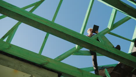 una arquitecta está trabajando con una tableta entre las vigas de la supervisión arquitectónica del techo