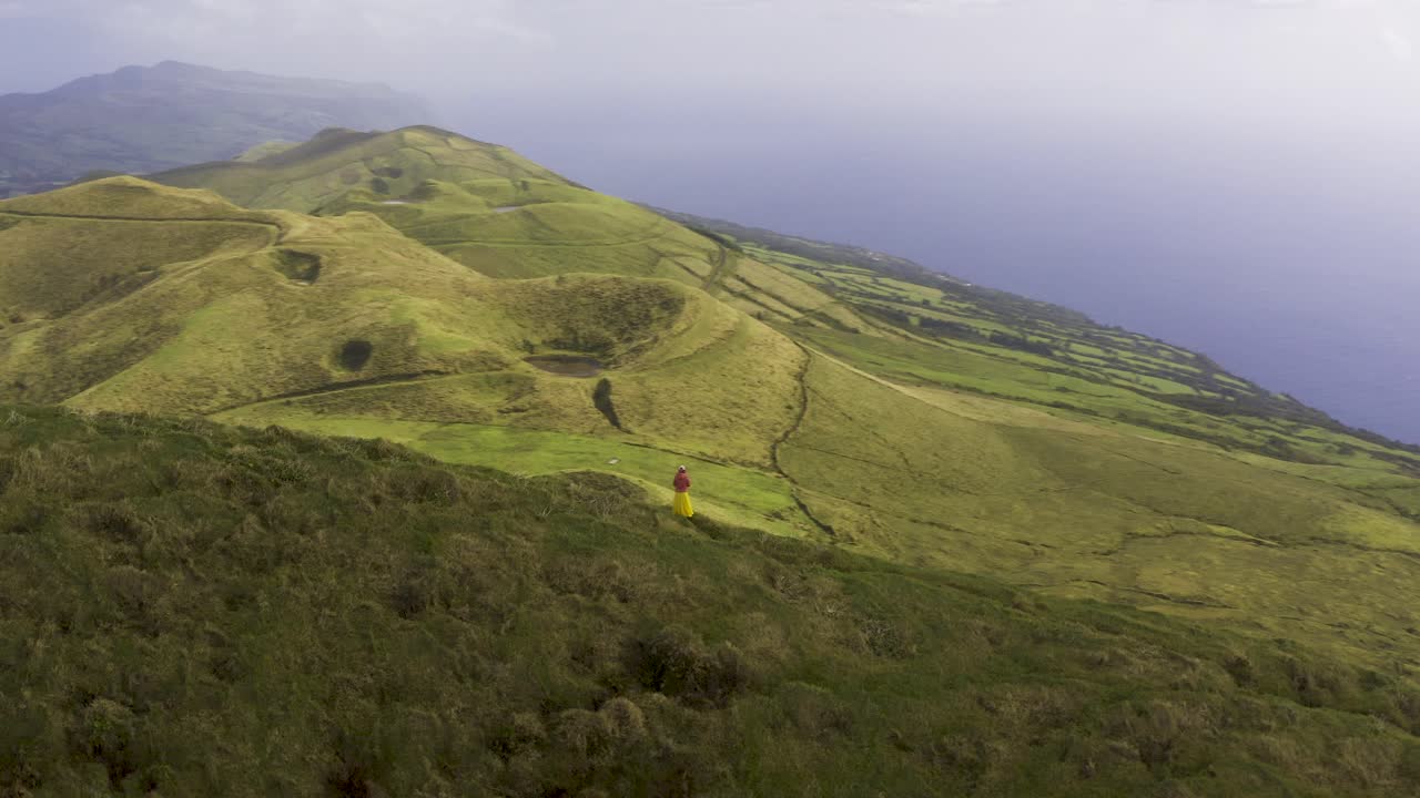 Drone mengorbit wanita turis Asia Malaysia Tiongkok yang sedang merekam video dengan ponsel di jalan setapak di tepi gunung, di Pico da Esperança, di pulau São Jorge, Azores, Portugal