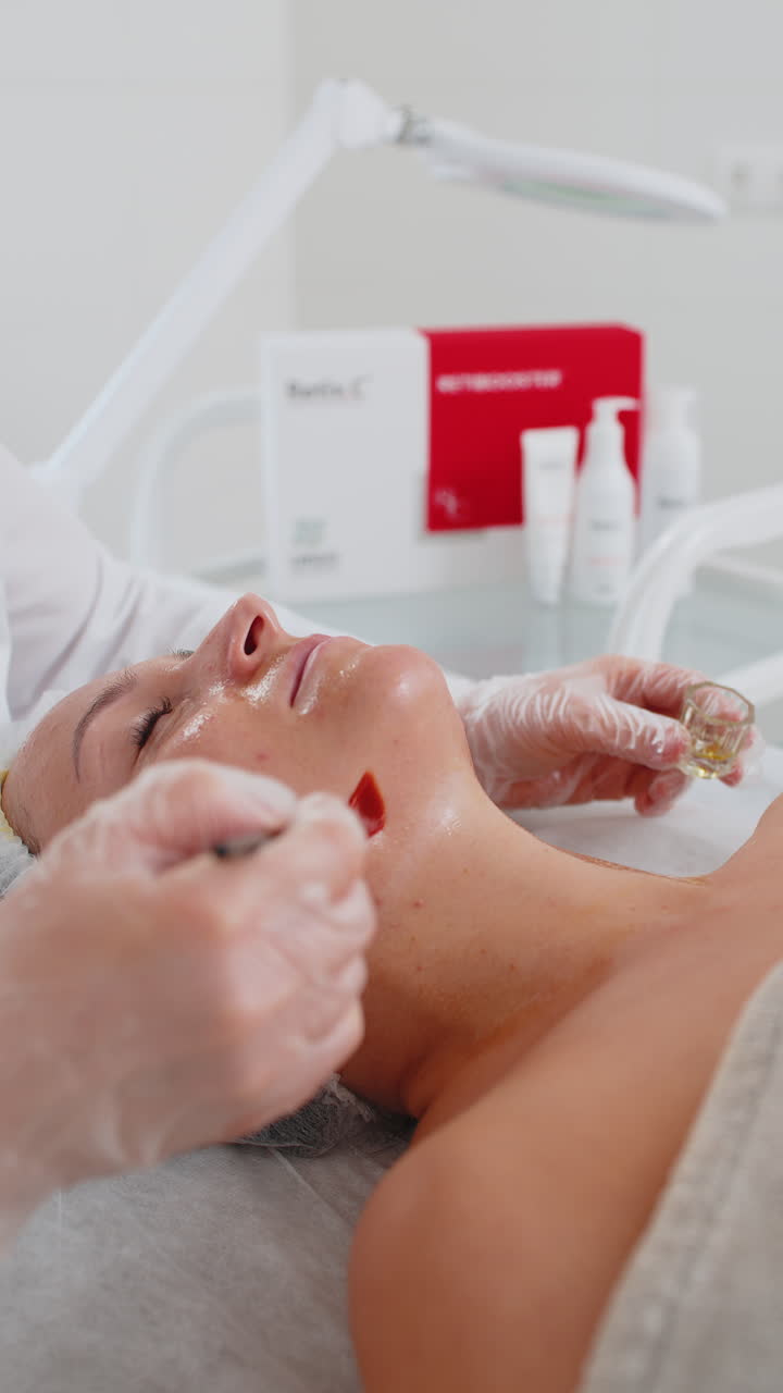Estetista che applica una crema medica idratante sul collo di una giovane donna con un pennello durante un trattamento enzimatico