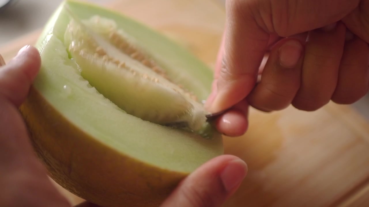 Close-up of Hands Scooping Seeds from a Fresh Honeydew Melon Half
