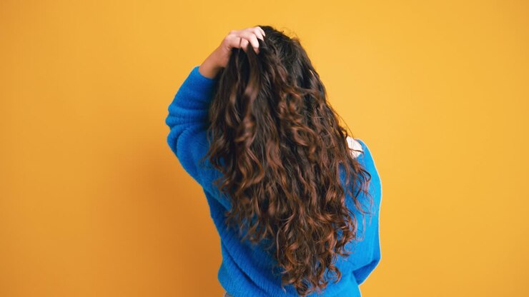 Vista trasera de mujer con cabello largo y rizado ajustándoselo