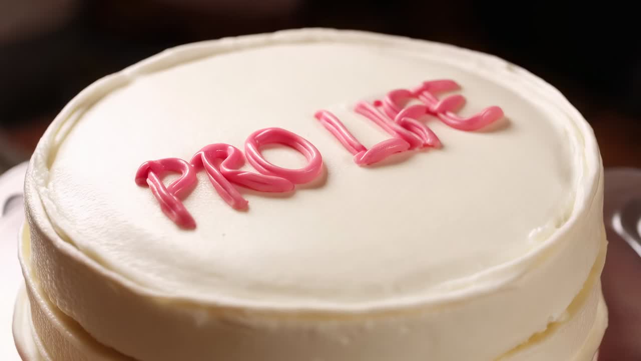 Rotazione della camera che cattura una torta rotonda a due strati su un tavolo, che mostra le lettere rosa PRO LIFE