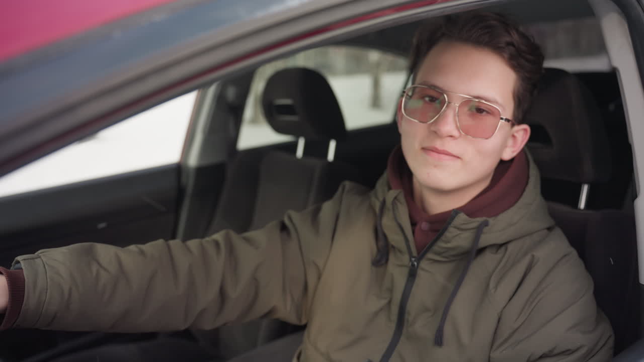 remote worker in winter jacket and glasses sits in car and rolls down window while smiling at camera through open side creating relaxed atmosphere with soft focus and muted winter background