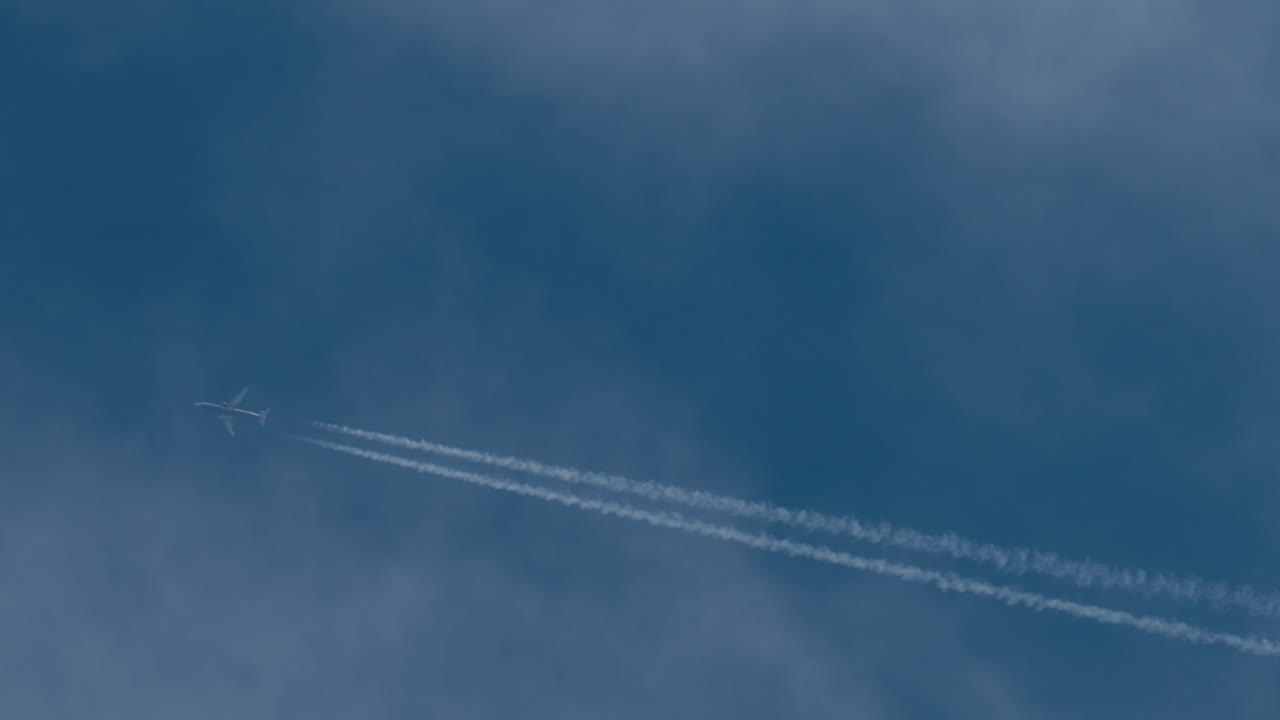 Airplane flying high above leaving long contrails in a clear blue sky