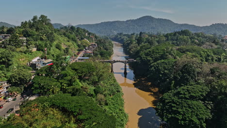 Peradeniya-Sri-Lanka-Drone-Cinematográfico-Aéreo-V5-Vuela-A-Lo-Largo-Del-Río-Mahaweli-Ganga,-Sobrevuela-El-Puente-De-La-Carretera-Principal-A1-Capturando-Suburbios-En-Kandy-Y-Vistas-Del-Paisaje-De-Las-Laderas---Filmado-Con-Cine-Mavic-3---Abril-De-2023