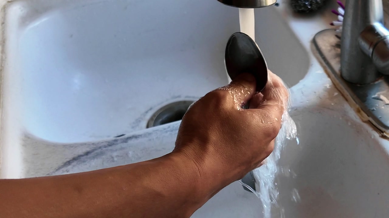 Rinsing the spoon with warm water for sanitization.