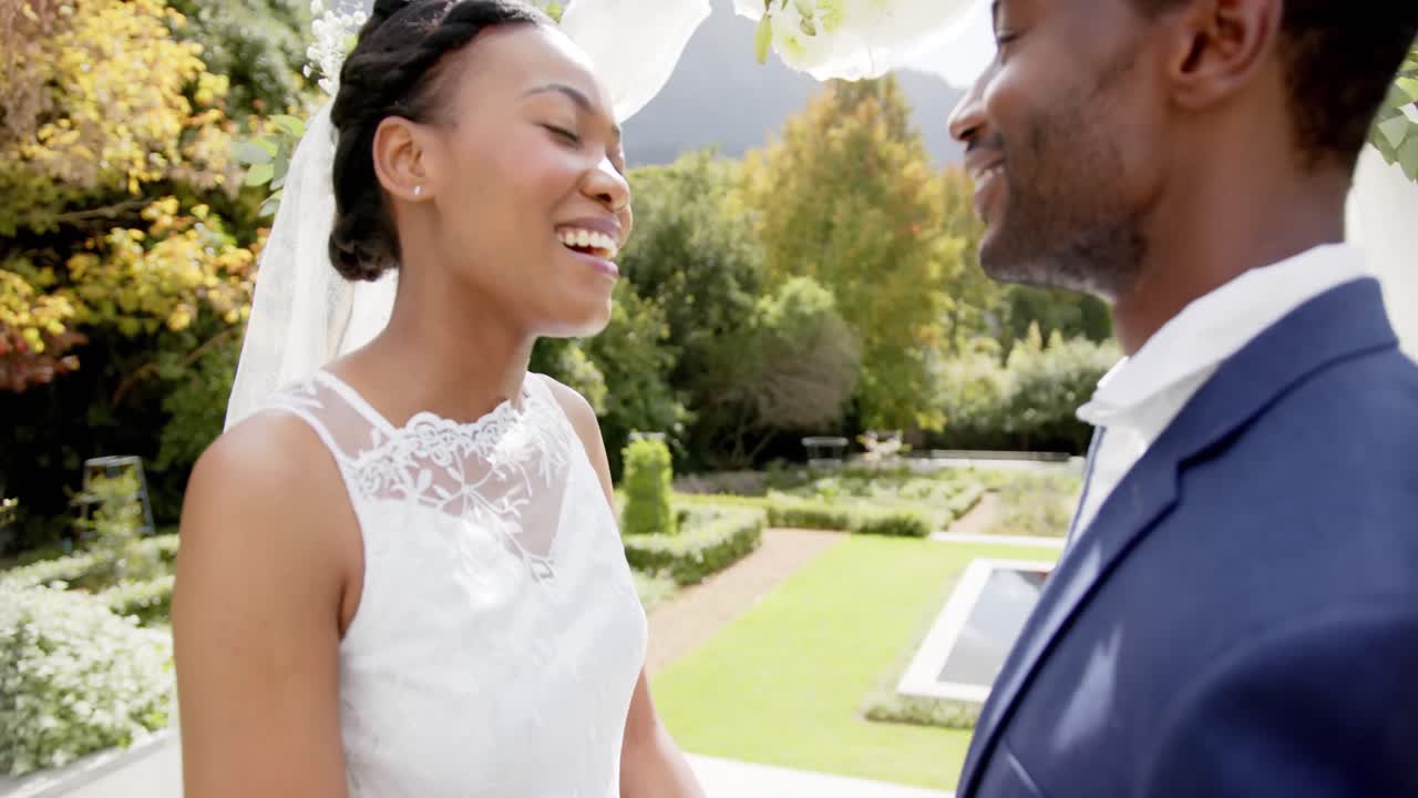 Happy african american couple smiling at each other at their wedding in sunny garden, in slow motion