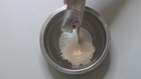 adding active instant dry yeast into a bowl of warm water, slow-motion video clip