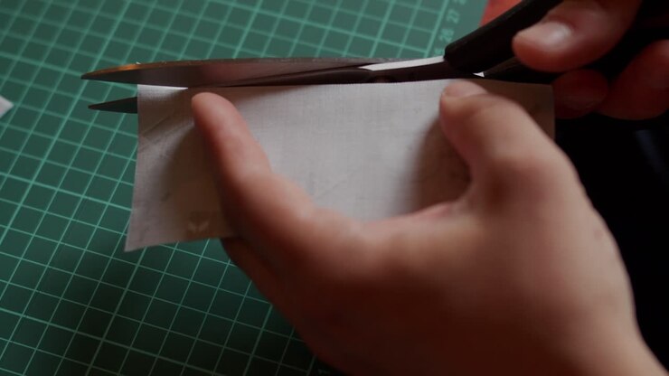 Holding a small piece of fabric and cutting it with scissors.